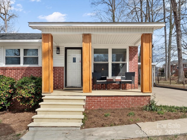 view of exterior entry featuring covered porch and brick siding