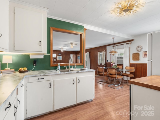 kitchen featuring light wood-style flooring, a sink, white cabinetry, light countertops, and crown molding