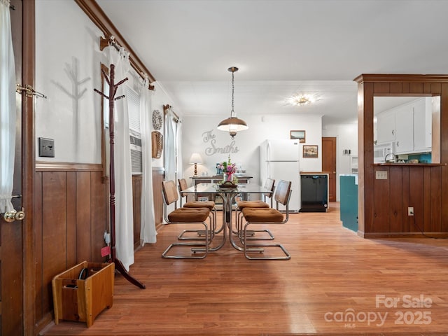 dining area with light wood finished floors, a wainscoted wall, and wood walls