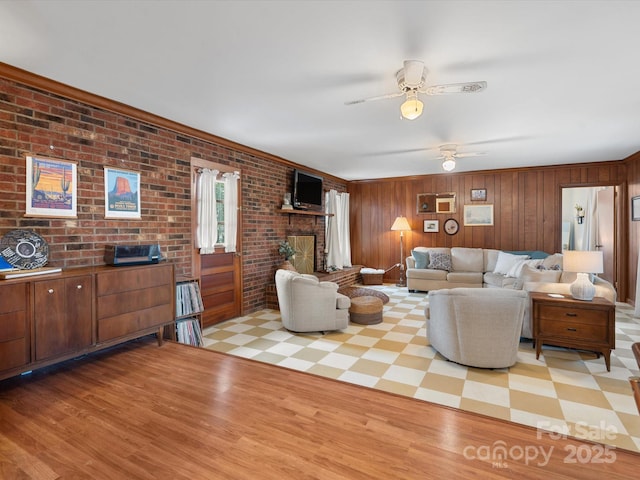 living area featuring brick wall, light wood finished floors, ceiling fan, and a brick fireplace