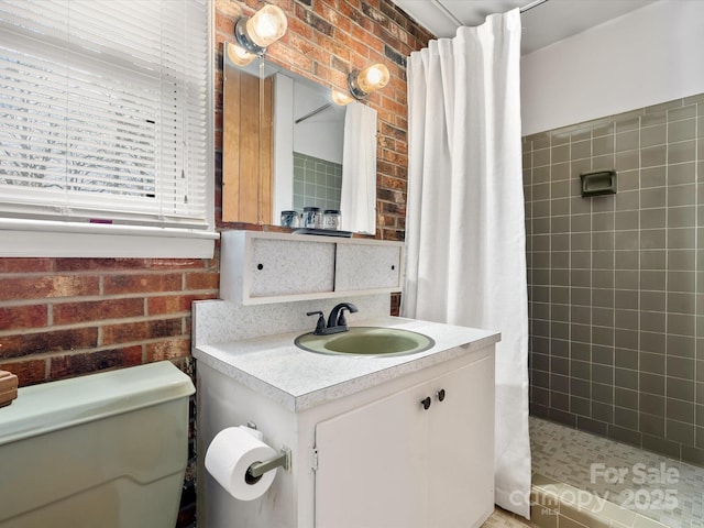 full bath featuring toilet, brick wall, tiled shower, and vanity