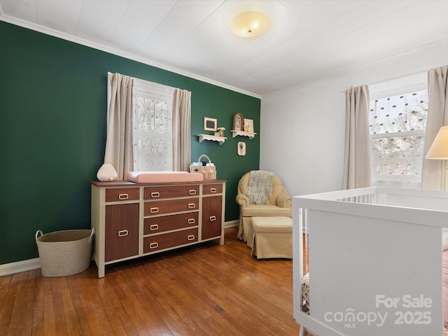 bedroom featuring dark wood-style floors, a nursery area, crown molding, and baseboards