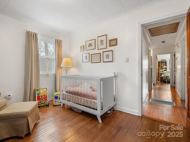 bedroom featuring ornamental molding, a nursery area, wood-type flooring, and baseboards