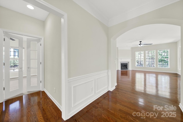 corridor featuring a wainscoted wall, plenty of natural light, wood finished floors, and arched walkways