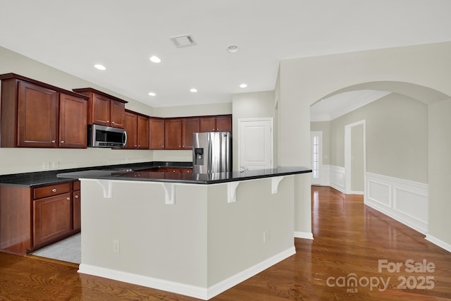 kitchen featuring dark countertops, visible vents, a kitchen breakfast bar, wood finished floors, and stainless steel appliances