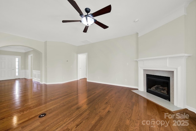 unfurnished living room with arched walkways, a fireplace with flush hearth, baseboards, and wood finished floors