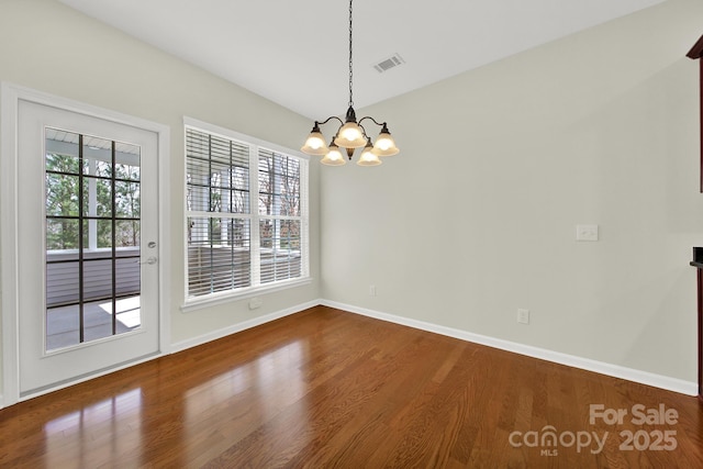 empty room featuring visible vents, baseboards, an inviting chandelier, and wood finished floors