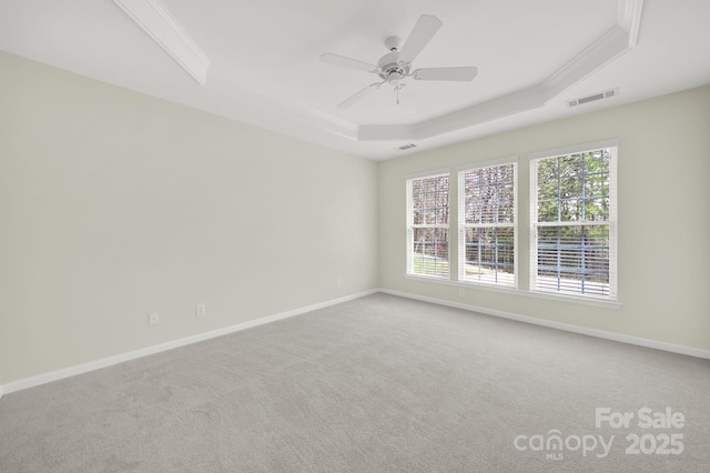 carpeted empty room featuring visible vents, baseboards, crown molding, a raised ceiling, and ceiling fan