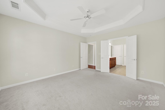 unfurnished bedroom featuring visible vents, ensuite bath, baseboards, a raised ceiling, and light colored carpet