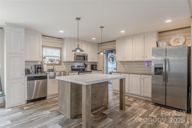 kitchen with a sink, wood finished floors, appliances with stainless steel finishes, and stacked washing maching and dryer