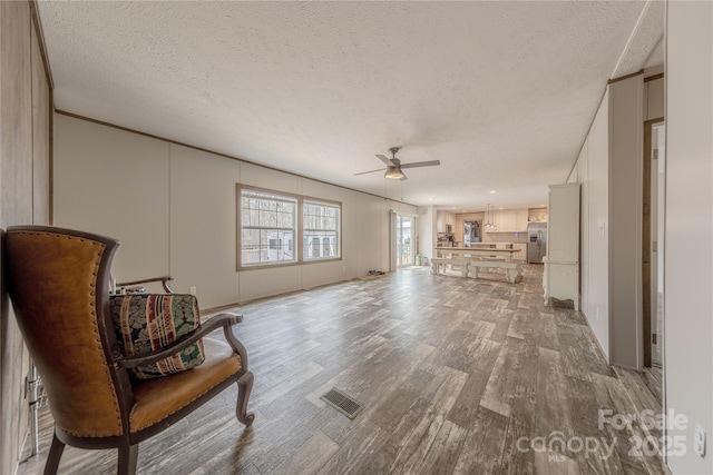 living room featuring visible vents, a textured ceiling, ceiling fan, and light wood finished floors