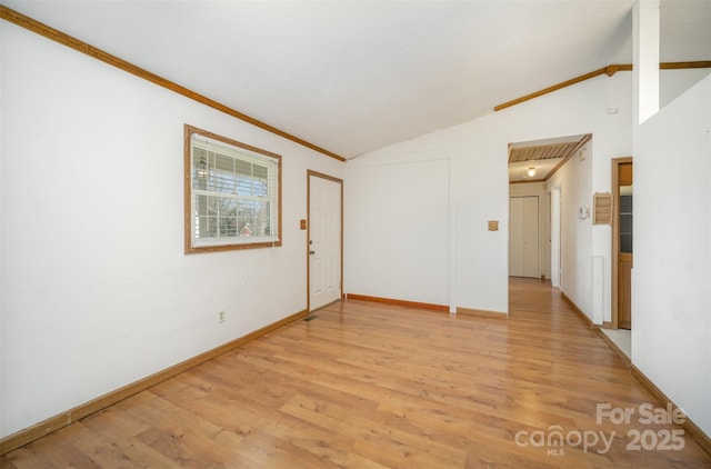 empty room featuring crown molding, light wood-type flooring, and vaulted ceiling