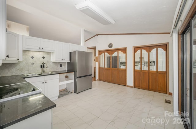 kitchen featuring lofted ceiling, dark countertops, freestanding refrigerator, white cabinetry, and a sink