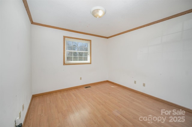 spare room featuring baseboards, wood finished floors, visible vents, and crown molding