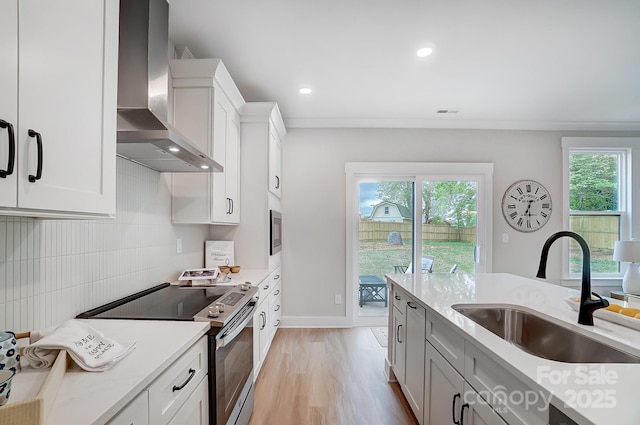 kitchen with wall chimney range hood, appliances with stainless steel finishes, a sink, light countertops, and light wood finished floors