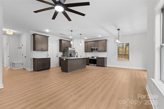 kitchen featuring a center island with sink, light countertops, decorative backsplash, appliances with stainless steel finishes, and dark brown cabinets