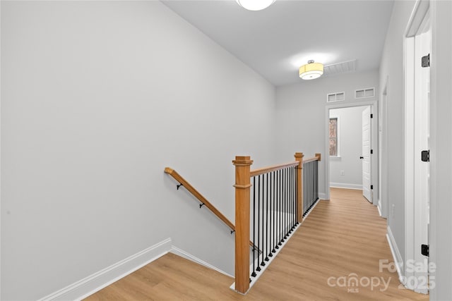 hall with baseboards, visible vents, light wood finished floors, and an upstairs landing