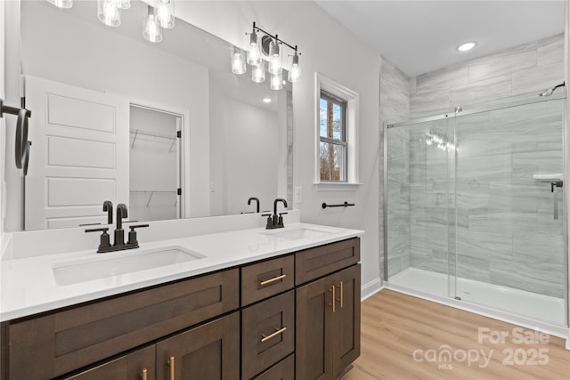 full bathroom with double vanity, wood finished floors, a sink, and a shower stall