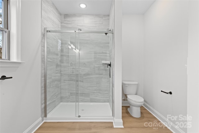 bathroom with toilet, a shower stall, baseboards, and wood finished floors