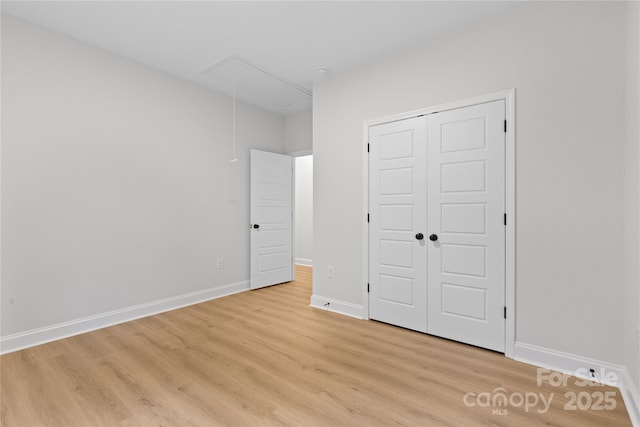 unfurnished bedroom featuring attic access, light wood-type flooring, a closet, and baseboards