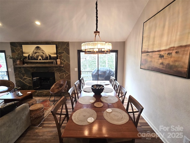 dining room featuring a chandelier, a stone fireplace, vaulted ceiling, and wood finished floors