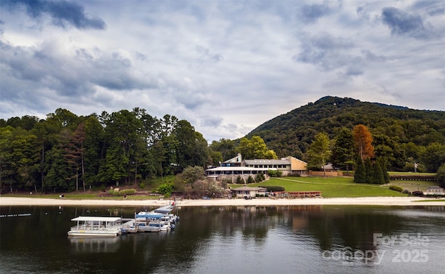 view of water feature featuring a floating dock, a mountain view, and a wooded view