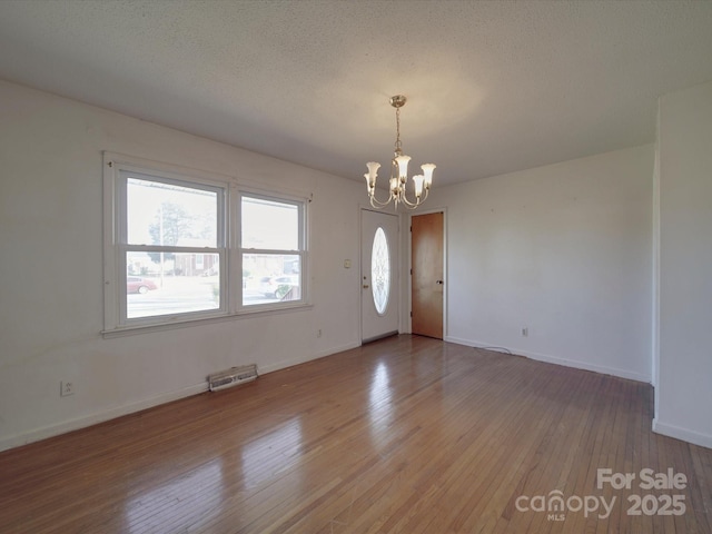 interior space with baseboards, light wood-style floors, a textured ceiling, and an inviting chandelier