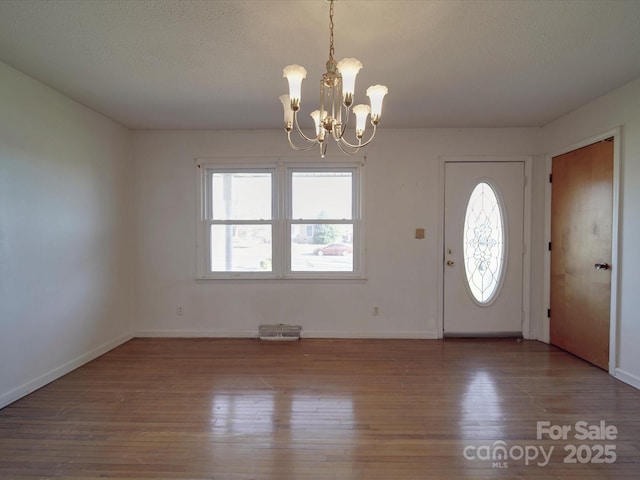 foyer with a chandelier, a textured ceiling, wood finished floors, and a healthy amount of sunlight