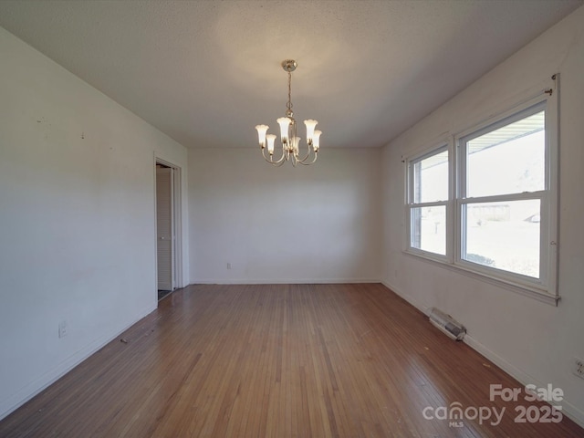 spare room with a notable chandelier, baseboards, and wood finished floors