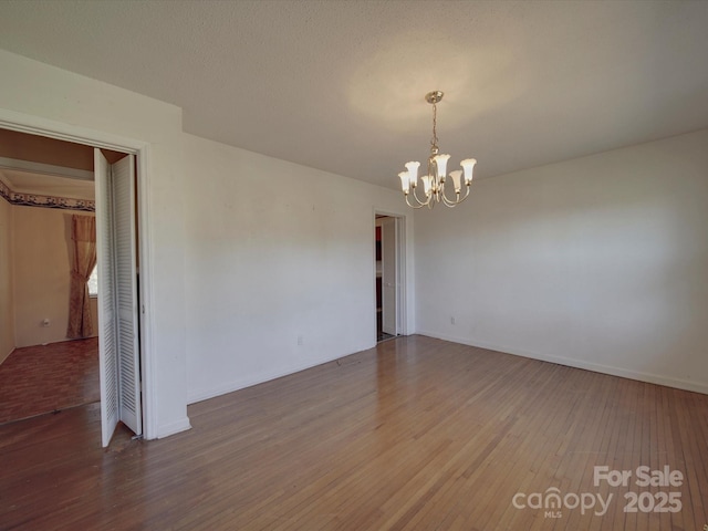 spare room with baseboards, wood finished floors, and an inviting chandelier