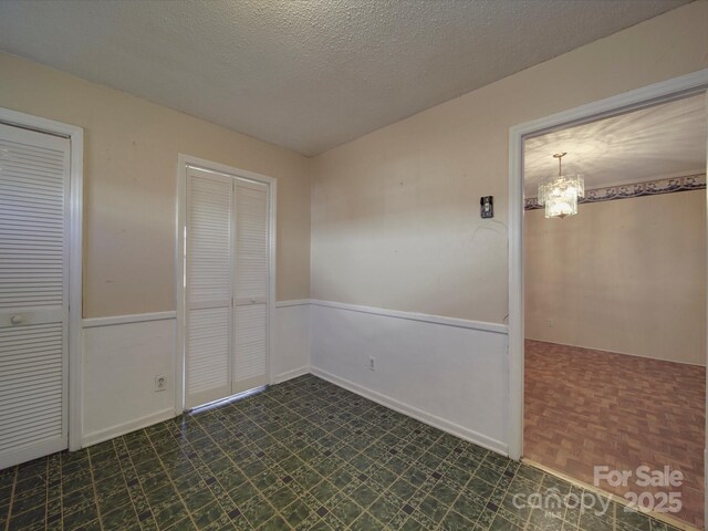 unfurnished bedroom featuring a textured ceiling, dark floors, and an inviting chandelier