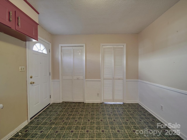 foyer entrance with a textured ceiling, dark floors, and wainscoting