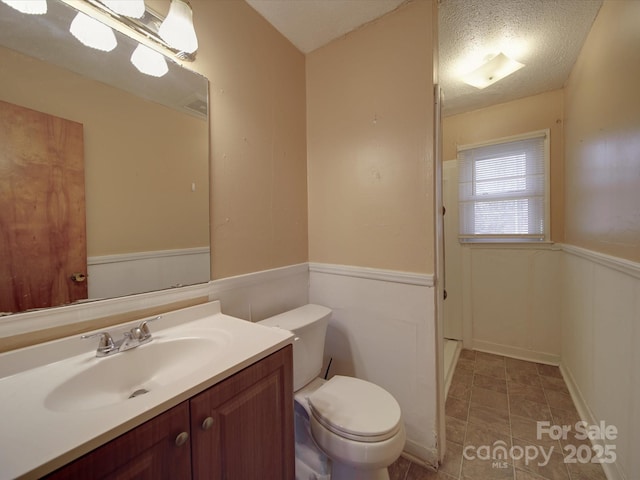 bathroom with a wainscoted wall, vanity, toilet, and a textured ceiling