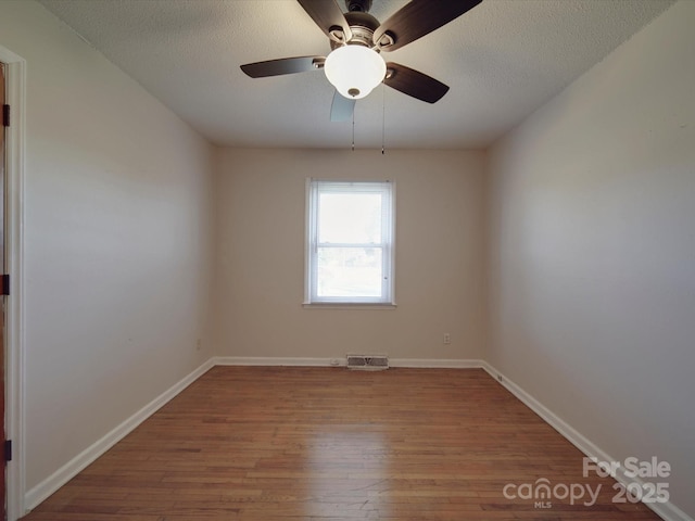 unfurnished room with visible vents, a textured ceiling, baseboards, and wood finished floors