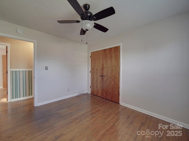 unfurnished bedroom featuring a closet, a textured ceiling, baseboards, and wood finished floors