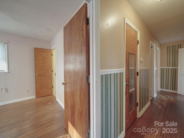 corridor with wood-type flooring, a textured ceiling, and baseboards