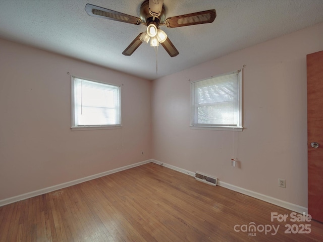 empty room with baseboards, visible vents, ceiling fan, wood finished floors, and a textured ceiling