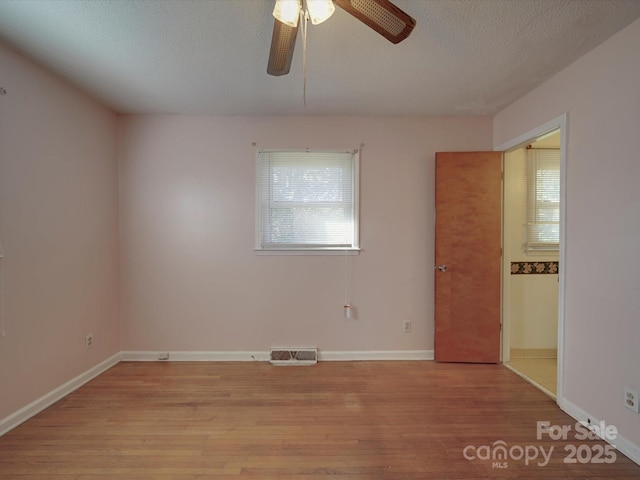 empty room featuring light wood-type flooring, plenty of natural light, visible vents, and a textured ceiling