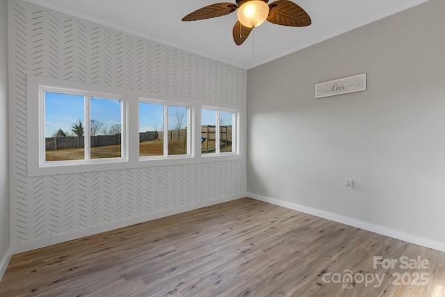 unfurnished room featuring a wealth of natural light, ceiling fan, baseboards, and wood finished floors