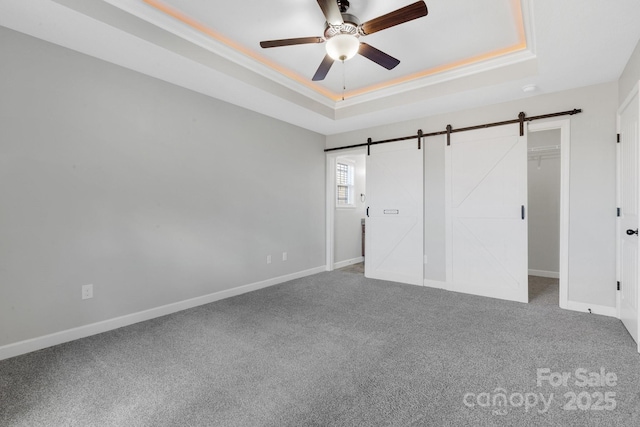 unfurnished bedroom with a barn door, a raised ceiling, and baseboards