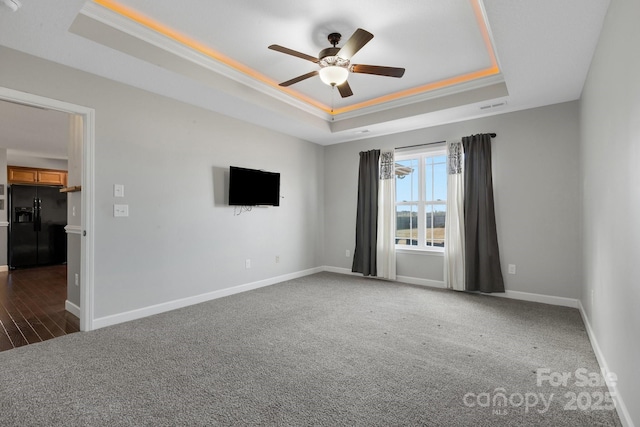 spare room with carpet floors, visible vents, a tray ceiling, and baseboards