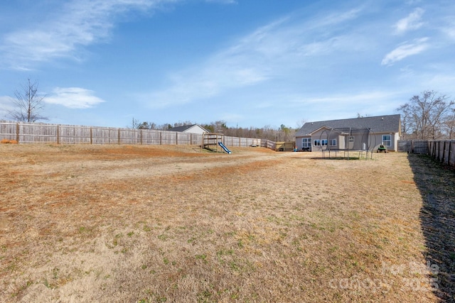 view of yard featuring a trampoline, a playground, and a fenced backyard