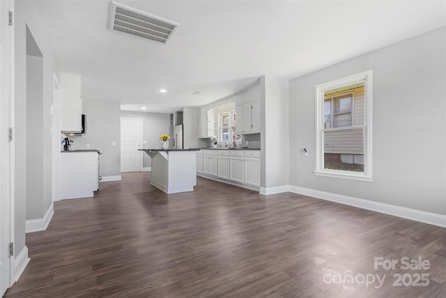 kitchen featuring baseboards, visible vents, dark wood finished floors, dark countertops, and a kitchen bar