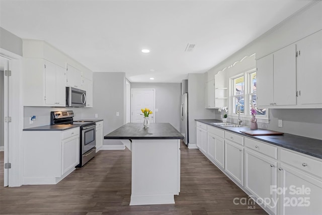 kitchen with stainless steel appliances, dark countertops, a sink, and white cabinetry