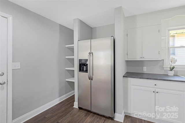 kitchen with dark countertops, dark wood-type flooring, white cabinets, stainless steel fridge, and baseboards