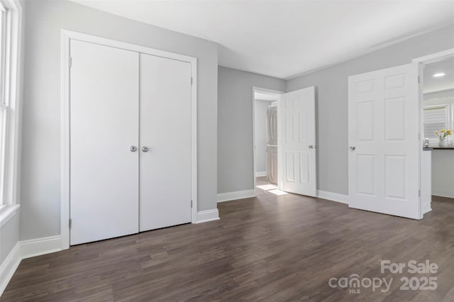 unfurnished bedroom featuring a closet, multiple windows, baseboards, and wood finished floors