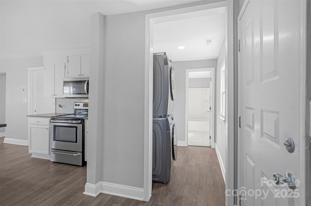 kitchen featuring white cabinetry, baseboards, stacked washer / drying machine, appliances with stainless steel finishes, and dark wood-style floors