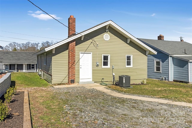 back of property with cooling unit, a lawn, and a chimney