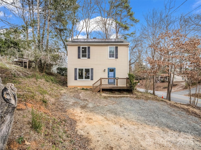 rear view of property with dirt driveway, solar panels, and a deck