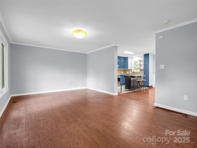 empty room featuring ornamental molding, wood finished floors, visible vents, and baseboards